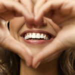 Closeup of a woman holding her hands in a heart shape in front of her beautiful smile after a smile redesign